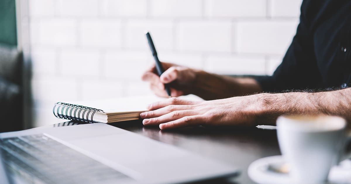 Mann sitzt am Schreibtisch und geht die Checkliste für den Immobilienkauf durch.