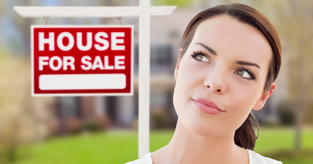 Frau überlegt vor einem Haus mit einem "Zu verkaufen"-Schild, wie sie im Alter wohnen möchte | Wohnen im Alter