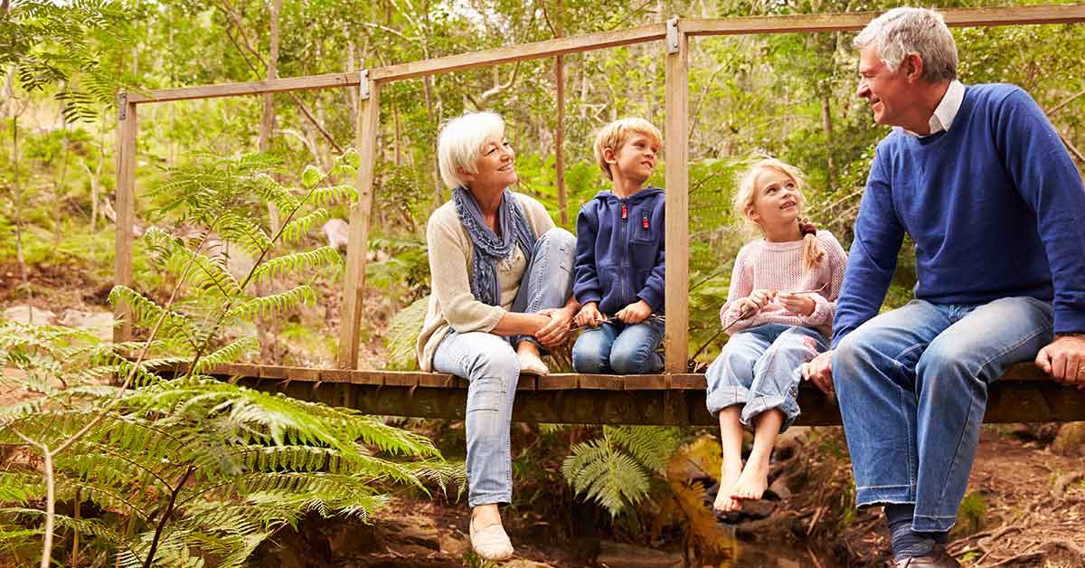 Großeltern sitzen mit Enkeln auf einer Holzbrücke im Wald - Wohnen im Alter