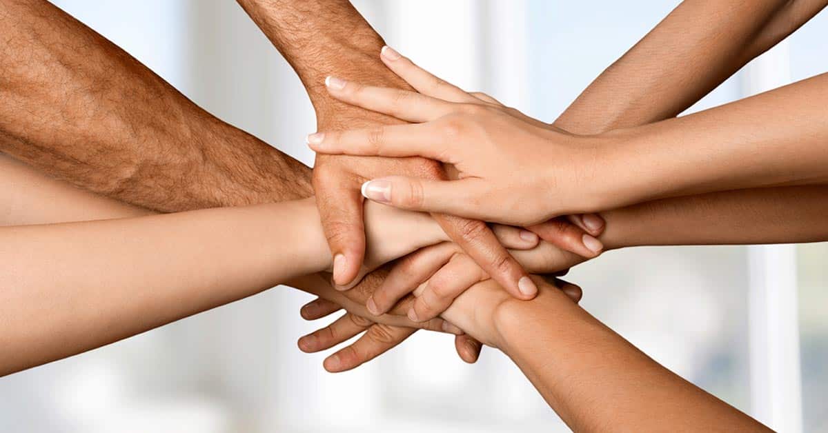 Mehrere Hände kommen zum Handschlag zusammen vor einem verschwommenen grauen und weißen Hintergrund - Erbimmobilien